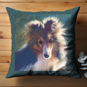 Könnte beinhalten: Ein blaues Zierkissen mit einer Aquarellmalerei eines Sheltie-Hundes mit braunem, weißem und schwarzem Fell. Der Hund schaut direkt auf den Betrachter. Das Kissen hat einen weißen Rand und den Text "Parnell Studios" in der rechten unteren Ecke.