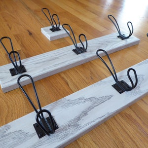 May include: Three white wooden coat racks with black metal hooks. The racks are different lengths and are arranged in a staggered pattern.