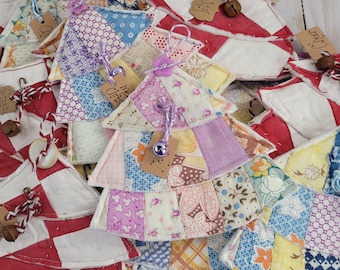 May include: A collection of fabric Christmas tree ornaments made from quilted patchwork squares in various floral and geometric patterns. Each ornament features a small hanging loop, a decorative button, a metal bell, and a brown paper tag.