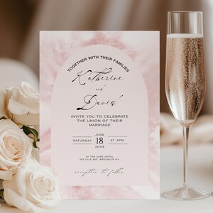 Op de afbeelding: Een huwelijksuitnodiging met een aquarel achtergrond in roze en witte tinten. De uitnodiging bevat de namen "Katherine en David" in een schrijflettertype en de tekst "Invite you to celebrate the union of their marriage" in een sans-serif lettertype. De datum en tijd van de bruiloft staan ​​eronder, samen met de locatie.