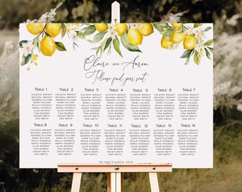 May include: A wedding seating chart on a wooden easel. The white sign features a lemon and floral design at the top, with the names "Claire and Aaron" and the words "Please find your seat." Tables 1-14 are listed with guest names.