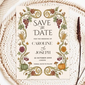 May include: A rectangular Save the Date card with cream background and black serif text. The border features detailed botanical illustrations of grapes, corn, pumpkins, mushrooms, and autumn leaves in muted green, orange, and brown tones.