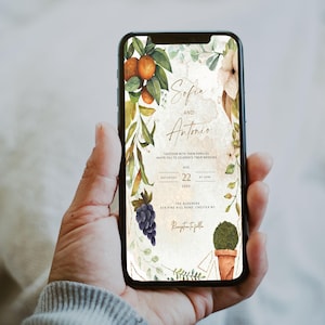 Puede incluir: Una invitación de boda con un diseño de acuarela que presenta una corona floral con naranjas, uvas y vegetación. El texto de la invitación dice "Sofia y Antonio" con la fecha y la ubicación de la boda.