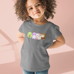 Puede incluir: Una camiseta gris de manga corta con un gráfico de cuatro personajes de dibujos animados. Los personajes son un aguacate, una criatura morada, una vaca y un mono. Los personajes son todos sonrientes y tienen expresiones amigables.