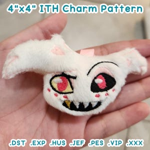 May include: A white plush charm with pink and red embroidered details, resembling a cartoon character. The charm is 4 inches by 4 inches and is labeled "ITH Charm Pattern".