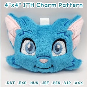 Puede incluir: Un amuleto de gato azul de felpa con detalles bordados, que incluyen ojos grandes y una nariz y orejas internas rosas. El amuleto mide aproximadamente 10 cm por 10 cm y tiene un lazo blanco para colgar. El texto "4"x4" ITH Charm Pattern" está en la parte superior.