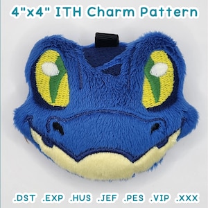 Op de afbeelding: Een geborduurd charme-patroon voor een 10 cm x 10 cm pluche speelgoed. Het patroon toont een blauw gezicht met grote gele ogen, een mond en een neus.