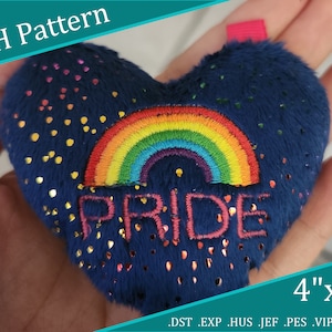 May include: A blue heart-shaped plush toy with a rainbow and the word "PRIDE" embroidered on it. The toy is 4 inches by 4 inches and has gold glitter accents.