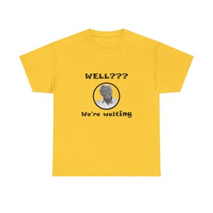 May include: A yellow t-shirt with the text "WELL???" above a circular image of a man, and the words "We're waiting" below. The shirt is a solid yellow color.