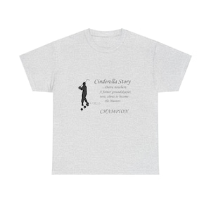 May include: A heather grey t-shirt with a black silhouette of a golfer and the text "Cinderella Story...Outta nowhere. A former groundskeeper, now, about to become the Masters CHAMPION".