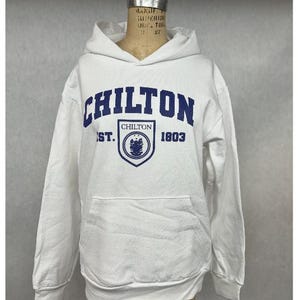 May include: White hooded sweatshirt with a front pocket and blue lettering that reads "CHILTON" above a crest and the text "EST. 1803". The sweatshirt is displayed on a mannequin.