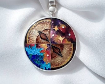 Pode incluir: Pingente de prata com um design circular dividido em quatro quadrantes. Um quadrante apresenta um céu estrelado, outro um oceano azul e turquesa, e os outros dois têm um esquema de cores marrom e dourado. O pingente tem um design de bússola.