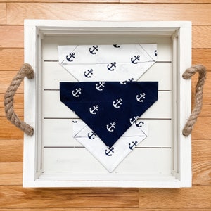 May include: Three white and blue bandana style dog bandanas with an anchor print. The bandanas are stacked on top of each other in a white tray with rope handles.
