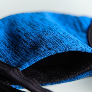 May include: A blue and black face mask with a textured fabric. The mask has a black elastic band for the ears.