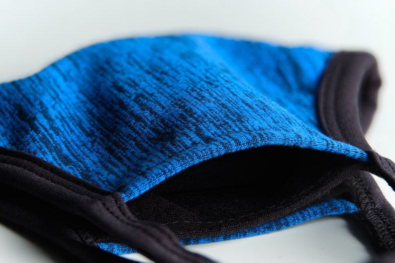 May include: A blue and black face mask with a textured fabric. The mask has a black elastic band for the ears.