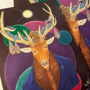 May include: Two art prints featuring a deer-like creature with antlers adorned with blue and white elements. The deer wears a blue jacket and has a brown beard. The background includes purple, green, and blue orbs, and a yellow sun.