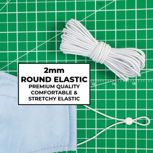 May include: White elastic cord, 2mm round, for sewing projects. The elastic is on a green cutting mat with a blue fabric mask and a white toggle.