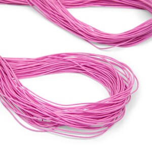 May include: A close-up of a spool of pink elastic cord. The cord is wound tightly and is ready to be used for crafting projects.