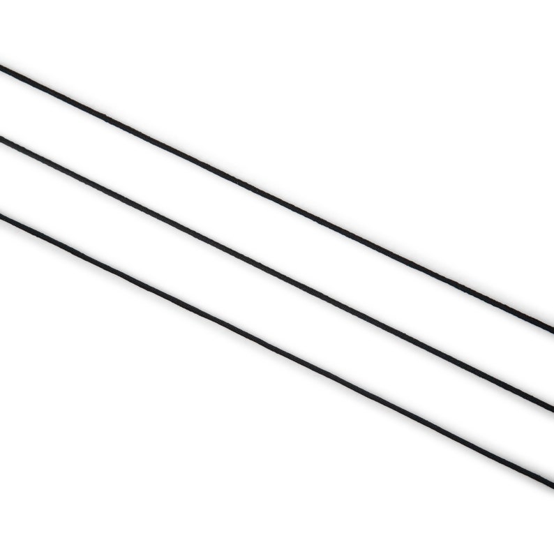 May include: Three thin, black cords are diagonally arranged against a white background. The cords appear to be made of a smooth, possibly synthetic material. The image is a simple, minimalist composition.