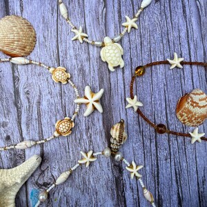 May include: Several necklaces and bracelets with a beach theme. The necklaces feature white starfish, turtle, and shell pendants, with white and gold beads. A few seashells are also visible.