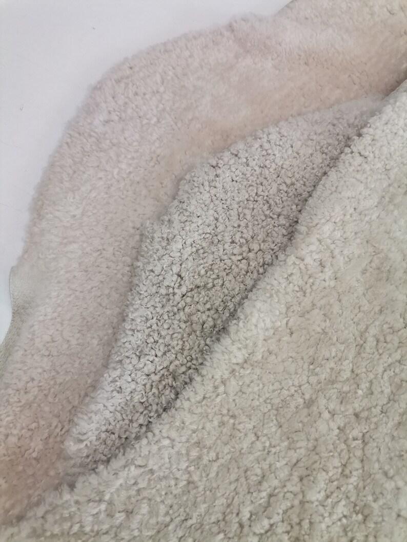 May include: Two pieces of soft, fluffy, white faux fur fabric. The fabric is folded in half, with the lighter side of the fabric on top.