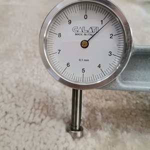 May include: A silver dial gauge with a white face and black markings. The gauge reads 0.1 mm and has the text "CALATI MADE IN ITALY" printed on the face.