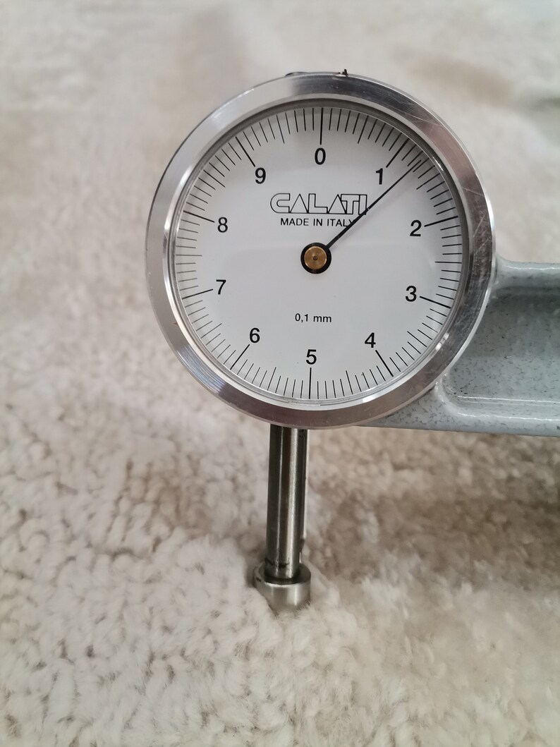 May include: A silver dial gauge with a white face and black markings. The gauge reads 0.1 mm and has the text "CALATI MADE IN ITALY" printed on the face.