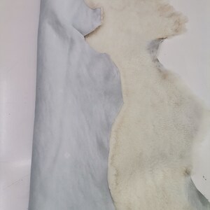May include: A white sheepskin with a light blue leather backing. The sheepskin is folded in half, showing both the fur and the leather.