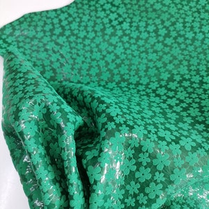 May include: Green fabric with a small white floral pattern. The fabric is textured and has a slight sheen.