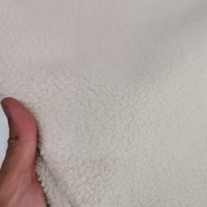 May include: Close-up of a white, fluffy fabric with a soft, fuzzy texture. The fabric is likely a type of fleece or sherpa.