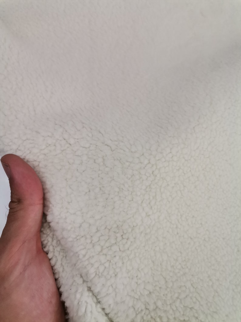 May include: Close-up of a white, fluffy fabric with a soft, fuzzy texture. The fabric is likely a type of fleece or sherpa.