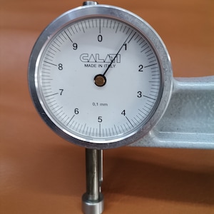 Peut inclure: Une jauge &agrave; cadran argent&eacute;e avec un cadran blanc et des marques noires. La jauge indique 0,1 mm et porte l'inscription "CALAVI MADE IN ITALY" sur le cadran.