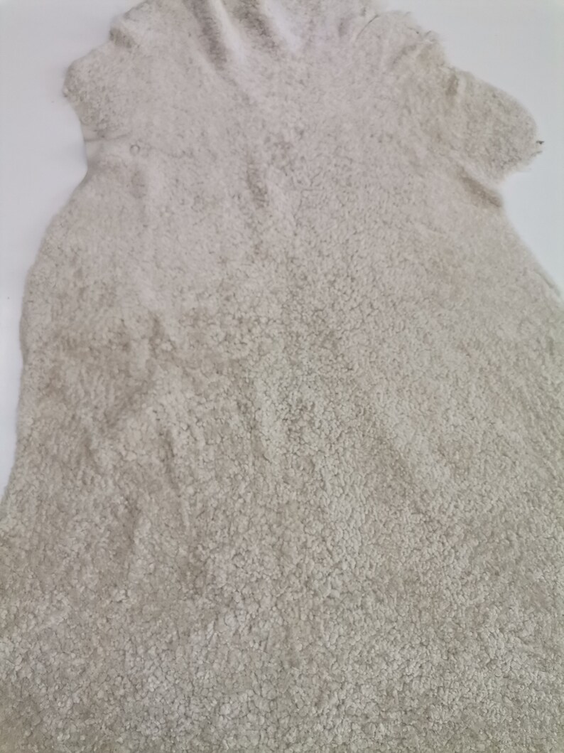 May include: A light beige sheepskin rug with a soft, fluffy texture.