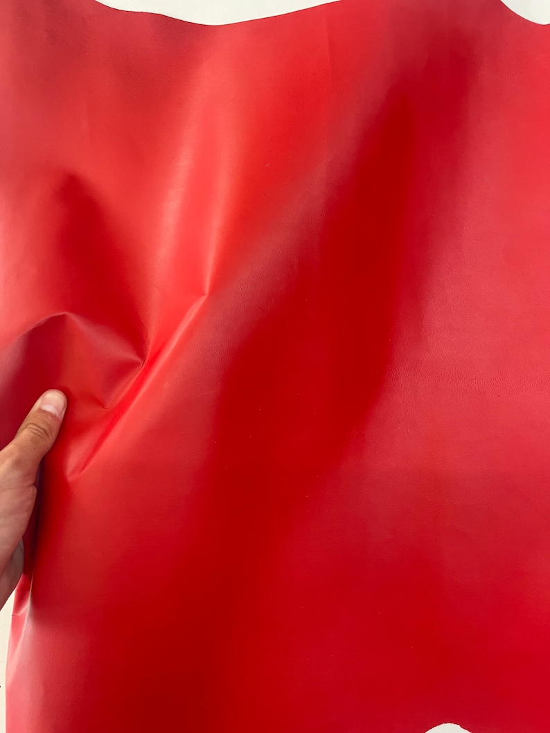 Puede incluir: Un trozo de cuero rojo brillante, doblado y texturizado, con una mano sujetando la esquina.