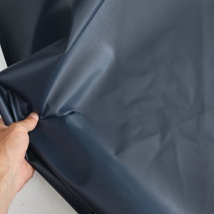 K&ouml;nnte beinhalten: Ein dunkelblauer Stoff mit einer glatten, leicht gl&auml;nzenden Oberfl&auml;che. Der Stoff ist gefaltet und wird in einer Hand gehalten.