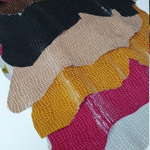 May include: A stack of eight different colored faux leather sheets with a crocodile skin pattern. The colors are burgundy, brown, black, beige, yellow, pink, gray, and brown.