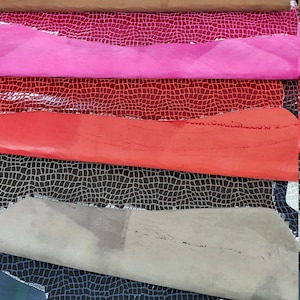 May include: A stack of five different colored leather samples. The leather has a textured, crocodile-like pattern. The colors are brown, pink, red, gray, and blue.