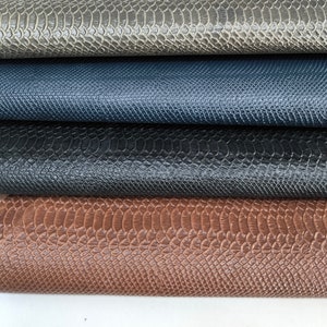 Op de afbeelding: Vier verschillende kleuren kunstleer met slangenhuidprint, op elkaar gestapeld. De kleuren zijn grijs, blauw, zwart en bruin.