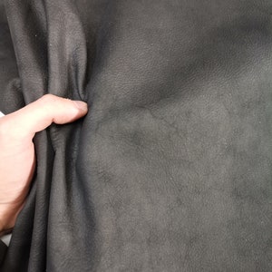 May include: Close-up of a dark gray leather material. The leather has a textured surface and is folded in half.