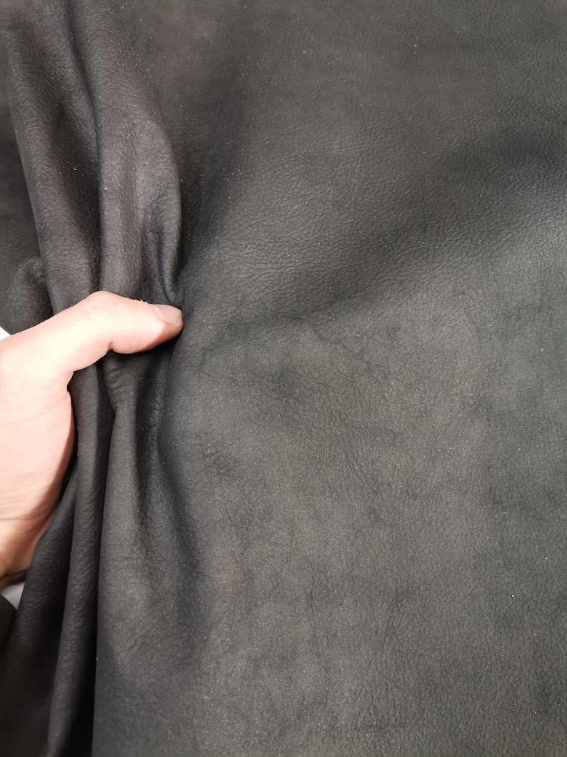 May include: Close-up of a dark gray leather material. The leather has a textured surface and is folded in half.