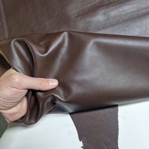 Peut inclure: Gros plan sur une peau de cuir marron. Le cuir est doux et souple, avec un motif de grain naturel. Il est pli&eacute; en deux, r&eacute;v&eacute;lant le dessous.