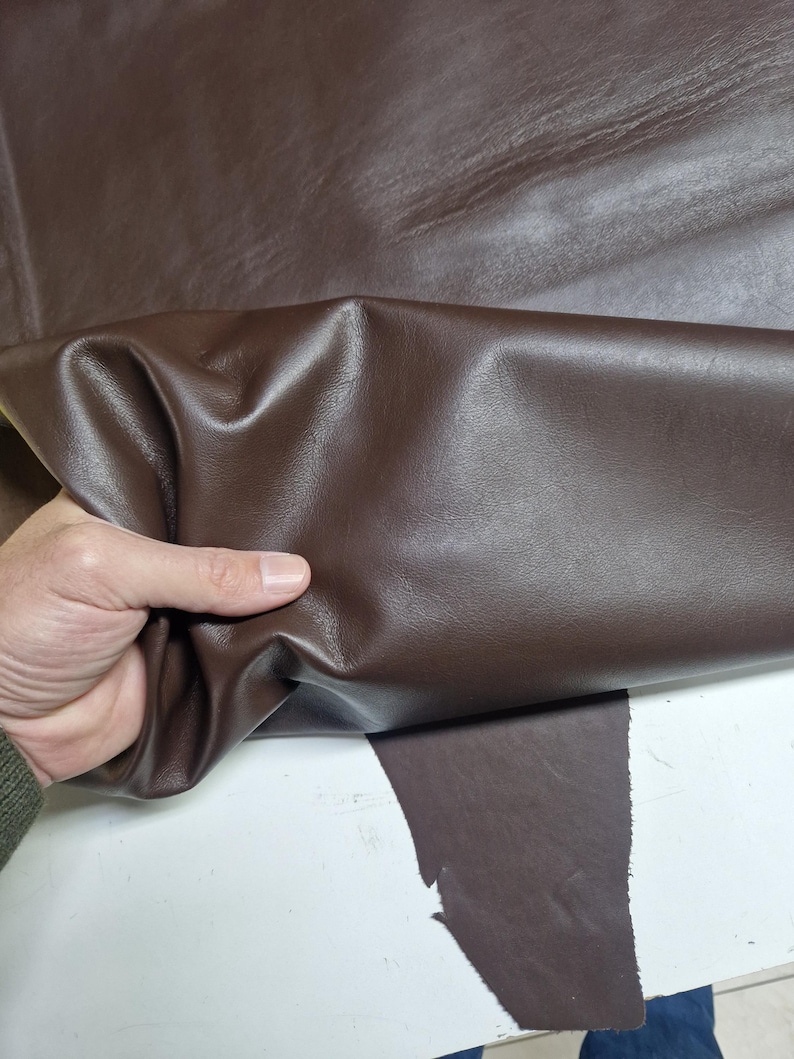 Peut inclure: Gros plan sur une peau de cuir marron. Le cuir est doux et souple, avec un motif de grain naturel. Il est pli&eacute; en deux, r&eacute;v&eacute;lant le dessous.