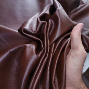 Peut inclure: Gros plan sur une peau de cuir marron fonc&eacute;, pli&eacute;e et drap&eacute;e, mettant en valeur sa texture lisse et son grain naturel.