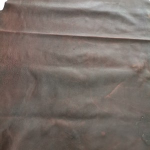以下が含まれることがあります： 滑らかで質感のある茶色の革の1枚。革はいくつかの場所で折り畳まれており、自然な木目と色の変化が見られます。