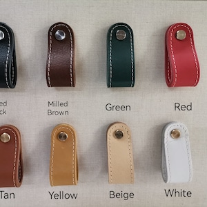 May include: Eight leather drawer pulls in various colors, including black, brown, green, red, tan, yellow, beige, and white. Each pull has a stitched edge and a metal knob.