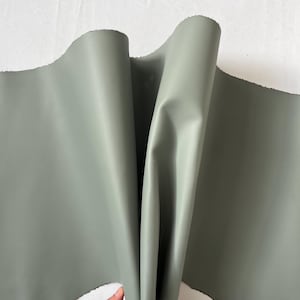 Puede incluir: Un trozo de cuero suave, flexible y verde. El cuero est&aacute; doblado por la mitad y sostenido por una mano.
