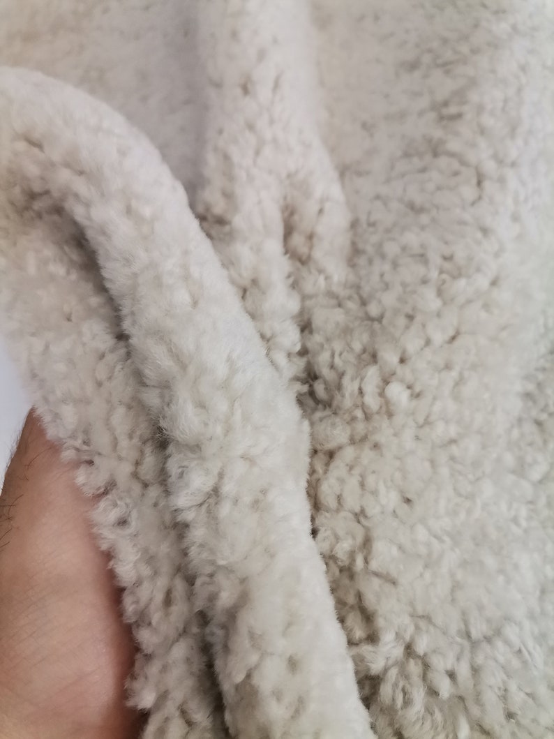 May include: Close-up of a soft, white, fluffy fabric with a textured surface. The fabric is folded in half, showing the texture of the material.