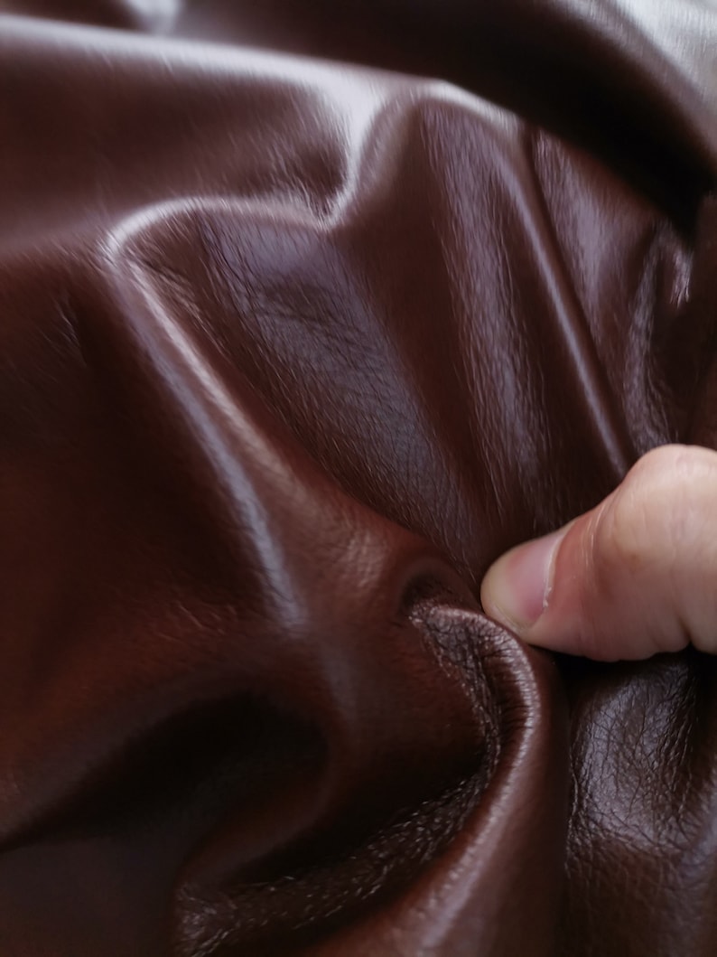Peut inclure: Gros plan sur un mat&eacute;riau en cuir brun fonc&eacute; avec une surface lisse et textur&eacute;e. Le cuir est pli&eacute; et froiss&eacute;, montrant sa flexibilit&eacute;.