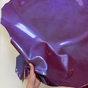 May include: A piece of iridescent purple leather with a glossy finish. The leather is folded and held in a hand.