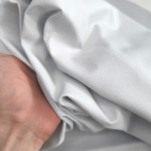 K&ouml;nnte beinhalten: Ein wei&szlig;er Stoff mit einer glatten, leicht strukturierten Oberfl&auml;che. Der Stoff ist gefaltet und zerknittert und zeigt seinen Fall und seine Flexibilit&auml;t.